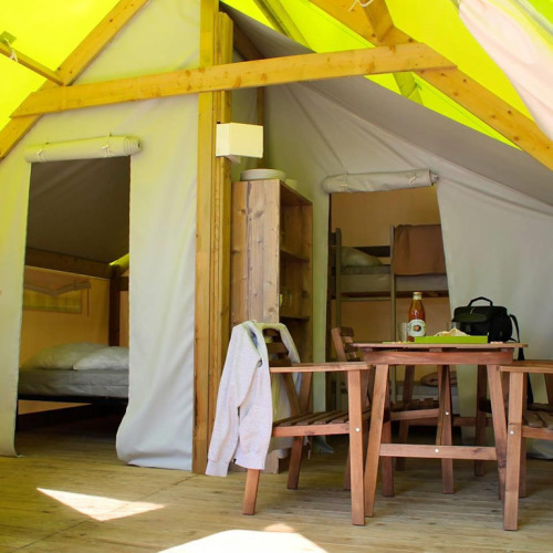 Intérieur d'une tente safari avec table à manger, chaises, étagère et espaces de couchage visibles