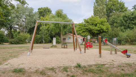 Parque infantil con columpios, balancín y juegos en la naturaleza en Camping Seasonova du Chêne, Pays de la Loire.