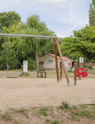 Parque infantil con columpios, balancín y juegos en la naturaleza en Camping Seasonova du Chêne, Pays de la Loire.