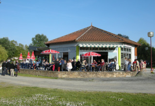 Feriepark i Pays de la Loire, Frankrig, med mennesker, der sidder udenfor en café under røde parasoller.