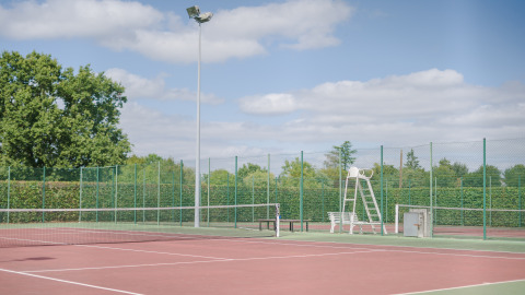 Pista de tenis al aire libre en Camping Seasonova du Chêne, rodeada de vallas y árboles en Pays de la Loire, Francia.