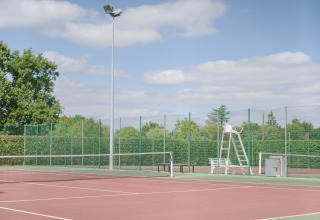 Udendørs tennisbane ved Camping Seasonova du Chêne, omgivet af hegn og træer i Pays de la Loire, Frankrig.