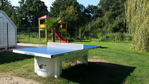 Mesa de ping pong al aire libre en Camping Seasonova du Chêne, con zona de juegos al fondo en Pays de la Loire.