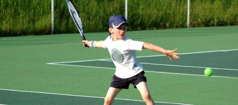 Jonge jongen speelt tennis op een buitenbaan bij Camping Seasonova du Chêne, Pays de la Loire, Frankrijk.