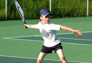 Jonge jongen speelt tennis op een buitenbaan bij Camping Seasonova du Chêne, Pays de la Loire, Frankrijk.