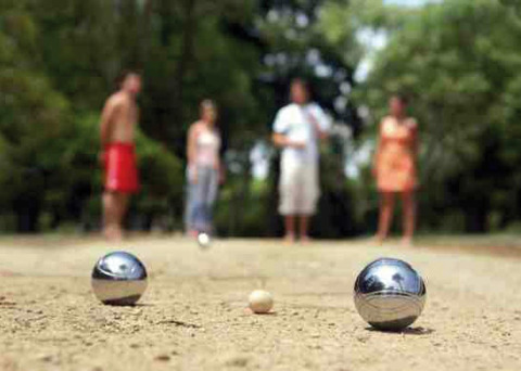Cuatro personas juegan a la petanca en una cancha de arena en Camping Seasonova du Chêne, Pays de la Loire, Francia.