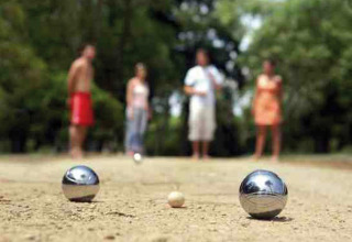 Four people play pétanque on a sandy pitch at Camping Seasonova du Chêne holiday park in Pays de la Loire, France.