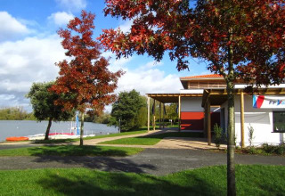 Herfstlandschap bij Camping Seasonova du Chêne in Pays de la Loire met meer, gebouw en gekleurde bomen.