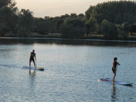 Two people paddleboarding on a calm lake at Camping Seasonova du Chêne in Pays de la Loire, France.