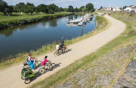 Senda ciclista junto al río en Camping Seasonova du Chêne, Pays de la Loire, Francia, con familias en bicicleta.