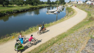 Senda ciclista junto al río en Camping Seasonova du Chêne, Pays de la Loire, Francia, con familias en bicicleta.