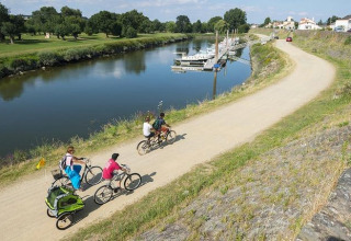 Senda ciclista junto al río en Camping Seasonova du Chêne, Pays de la Loire, Francia, con familias en bicicleta.