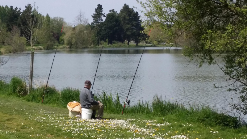A man fishing by the lake at Camping Seasonova du Chêne, Pays de la Loire, France, surrounded by nature.