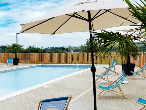 Piscina exterior con tumbonas azules, sombrillas y palmeras en Domaine Seasonova Saâne et Mer, Normandía, Francia.