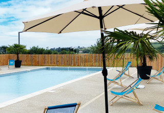 Buitenzwembad met blauwe ligstoelen, parasols en palmbomen bij Domaine Seasonova Saâne et Mer, Normandië, Frankrijk.