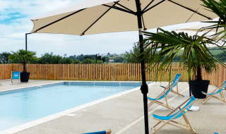 Piscina exterior con tumbonas azules, sombrillas y palmeras en Domaine Seasonova Saâne et Mer, Normandía, Francia.