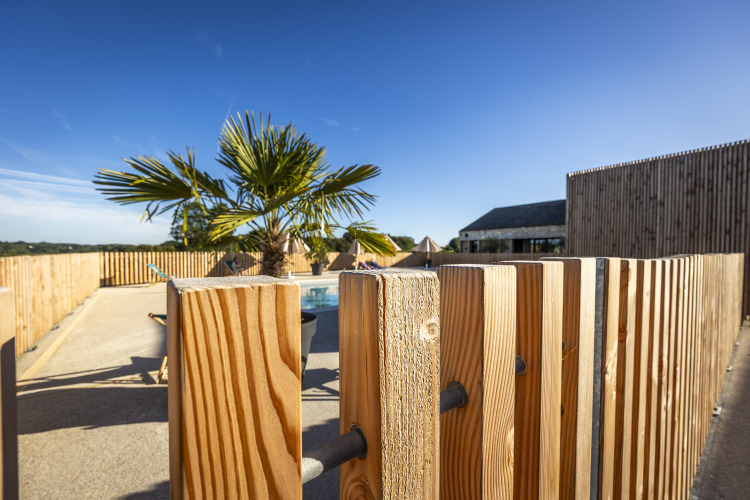 Outdoor pool area with palm tree and wooden fence under blue sky at Domaine Seasonova Saâne et Mer, Normandy.