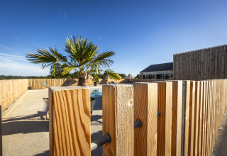 Espace piscine extérieur avec palmier et clôture en bois sous le ciel bleu à Domaine Seasonova Saâne et Mer, Normandie.