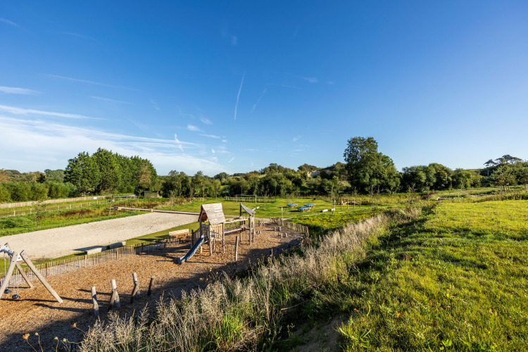 Playground and open green fields under a clear sky at Domaine Seasonova Saâne et Mer holiday park in Normandy, France.