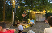 Udendørs koncert ved Camping Seasonova La Forêt i Pays de la Loire, Frankrig, med guitarist og publikum.