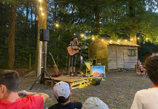 Udendørs koncert ved Camping Seasonova La Forêt i Pays de la Loire, Frankrig, med guitarist og publikum.
