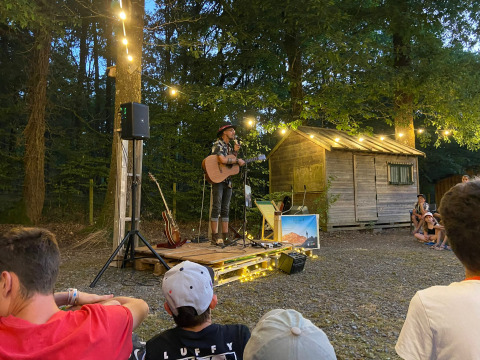 Udendørs koncert ved Camping Seasonova La Forêt i Pays de la Loire, Frankrig, med guitarist og publikum.