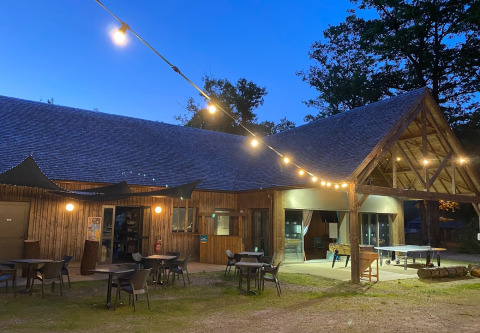 Abendliches Bild vom Camping Seasonova La Forêt in Pays de la Loire, Frankreich, mit Lichterketten und Terrasse.