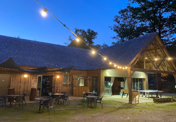 Abendliches Bild vom Camping Seasonova La Forêt in Pays de la Loire, Frankreich, mit Lichterketten und Terrasse.