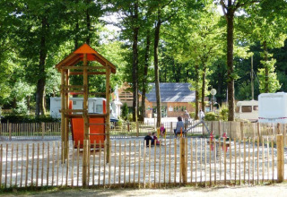 Speelterrein met toren en glijbaan bij Camping Seasonova La Forêt, Pays de la Loire, Frankrijk, omringd door bomen.