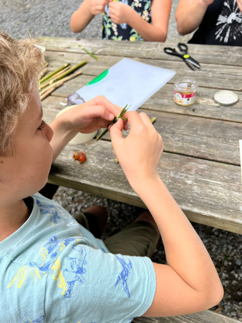 Niños haciendo manualidades con plantas en una mesa de madera en Camping Seasonova La Forêt, Pays de la Loire, Francia.