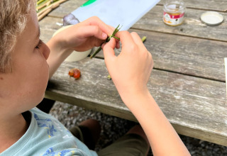 Børn laver håndværk med planter ved et træbord på Camping Seasonova La Forêt i Pays de la Loire, Frankrig.