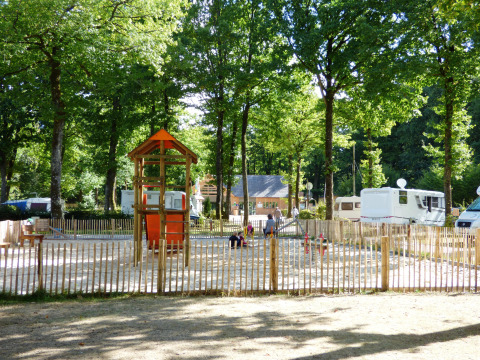 Speelplein met houten speeltoestellen en caravans tussen bomen op Camping Seasonova La Forêt, Frankrijk.