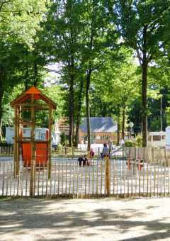 Parque infantil con estructuras de madera y caravanas entre árboles en Camping Seasonova La Forêt, Francia.