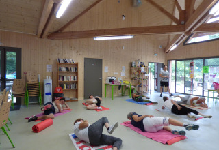 Persone partecipano a una lezione di ginnastica di gruppo su tappetini in una sala luminosa di legno al Camping Seasonova La Forêt.
