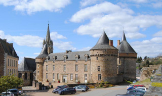 Castillo histórico en Sillé le Guillaume, Pays de la Loire, Francia, con torres y autos estacionados cerca.
