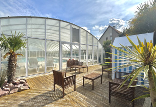 Buitenterras met palmbomen, zitplaatsen en een overdekt zwembad in een vakantiepark in Normandië, Frankrijk.