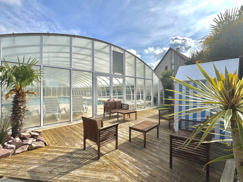 Terrasse extérieure avec palmiers, sièges et piscine couverte dans un parc de vacances en Normandie, France.