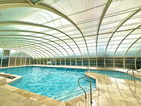 Piscina coperta con tetto arcuato trasparente al Camping Seasonova Le Point du Jour in Normandia, Francia.