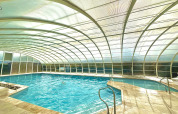 Indoor swimming pool with arched transparent roof at Camping Seasonova Le Point du Jour in Normandy, France.