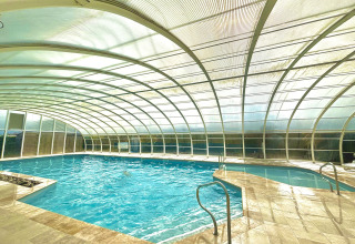 Piscina coperta con tetto arcuato trasparente al Camping Seasonova Le Point du Jour in Normandia, Francia.