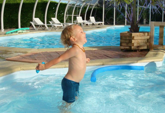 Bambino che gioca felice in piscina al Camping Seasonova Le Point du Jour, villaggio vacanze in Normandia, Francia.