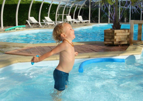 Niño pequeño juega feliz en la piscina del Camping Seasonova Le Point du Jour, parque vacacional en Normandía, Francia.