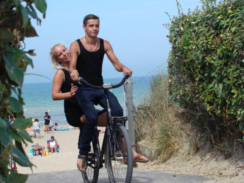 Een jong koppel fietst aan het strand op Camping Seasonova Le Point du Jour in Normandië, Frankrijk.