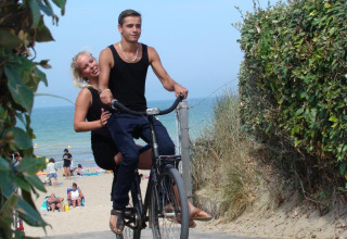 Een jong koppel fietst aan het strand op Camping Seasonova Le Point du Jour in Normandië, Frankrijk.