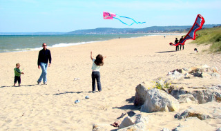 Des familles font voler des cerfs-volants sur une plage ensoleillée près de Merville Franceville Plage en Normandie.