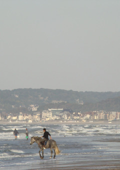 Cavalier sur la plage de Camping Seasonova Le Point du Jour en Normandie, France, avec vue sur la ville en arrière-plan.