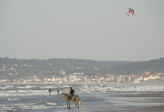 Cavalier sur la plage de Camping Seasonova Le Point du Jour en Normandie, France, avec vue sur la ville en arrière-plan.
