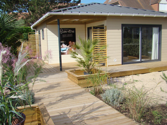 Holzterrasse und modernes Ferienhaus mit Pflanzen bei Camping Seasonova Le Point du Jour in der Normandie, Frankreich.