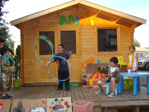 Bambini che giocano e recitano davanti a una casetta di legno al Camping Seasonova Le Point du Jour, Normandia.