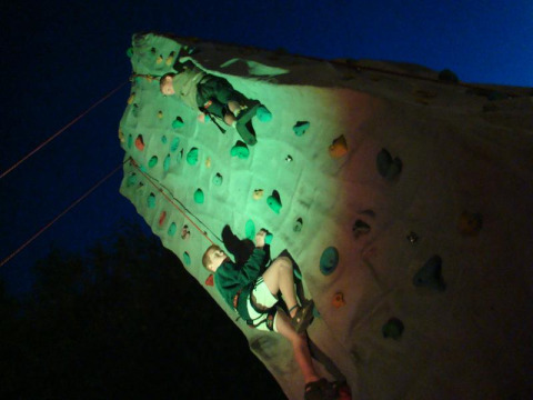 Twee kinderen beklimmen 's nachts een verlichte klimwand op Camping Seasonova Le Point du Jour in Normandië, Frankrijk.